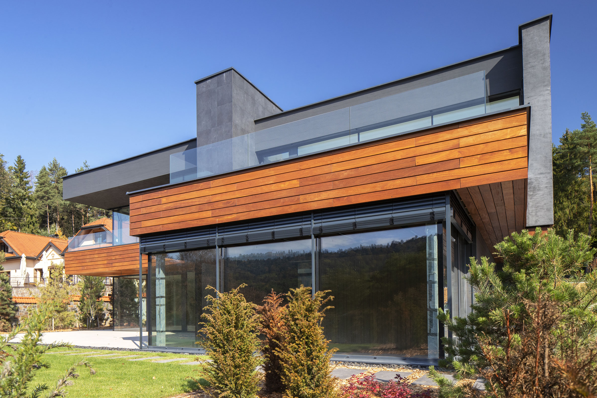 Dvojpodlažná vila upúta decentným kontrastom dreveného obkladu, skla a šedej brúsené omietky