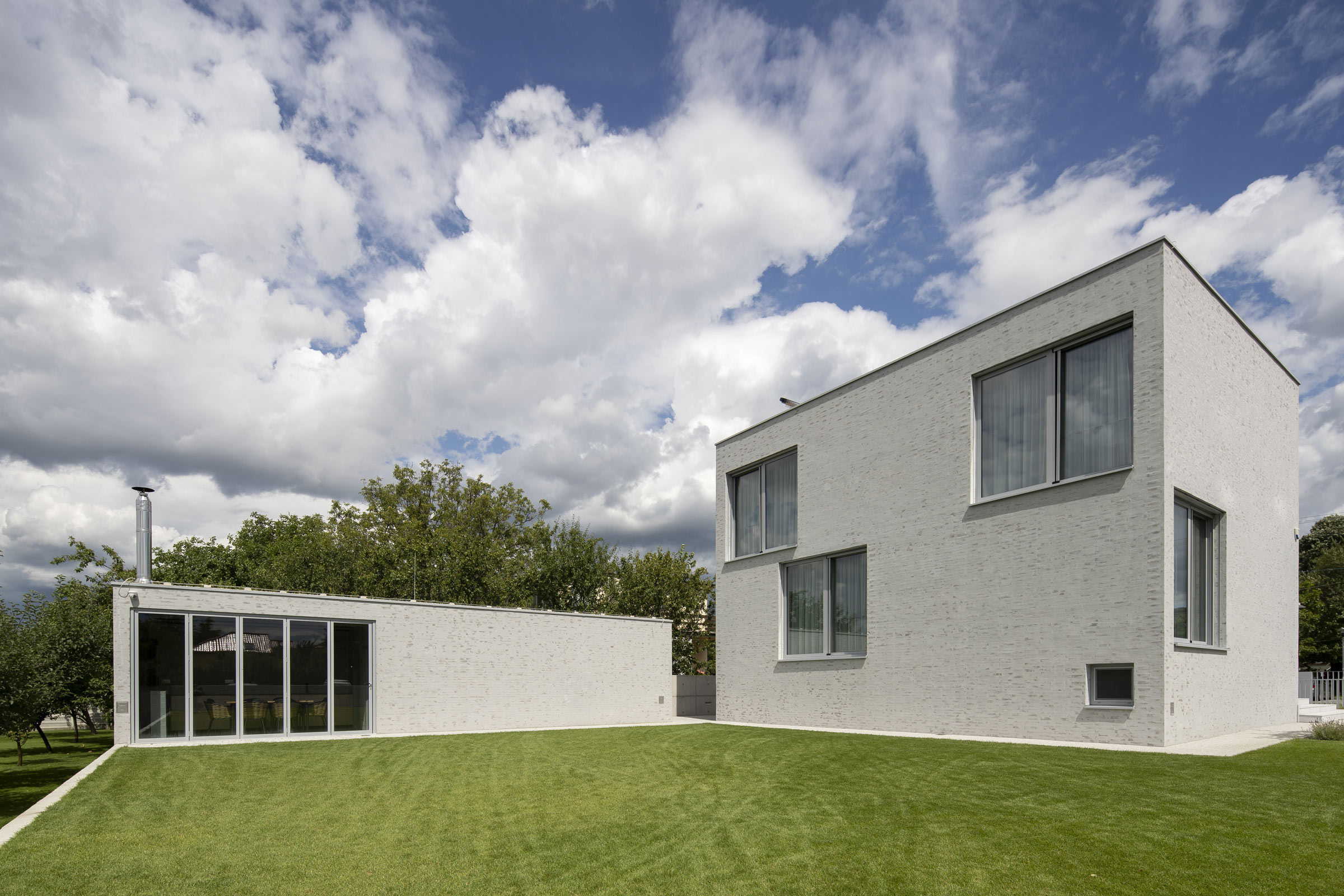 Fasáda rodinného domu z tehlového obkladu a brúsené omietky s jemnou, vrstvenou štruktúrou.